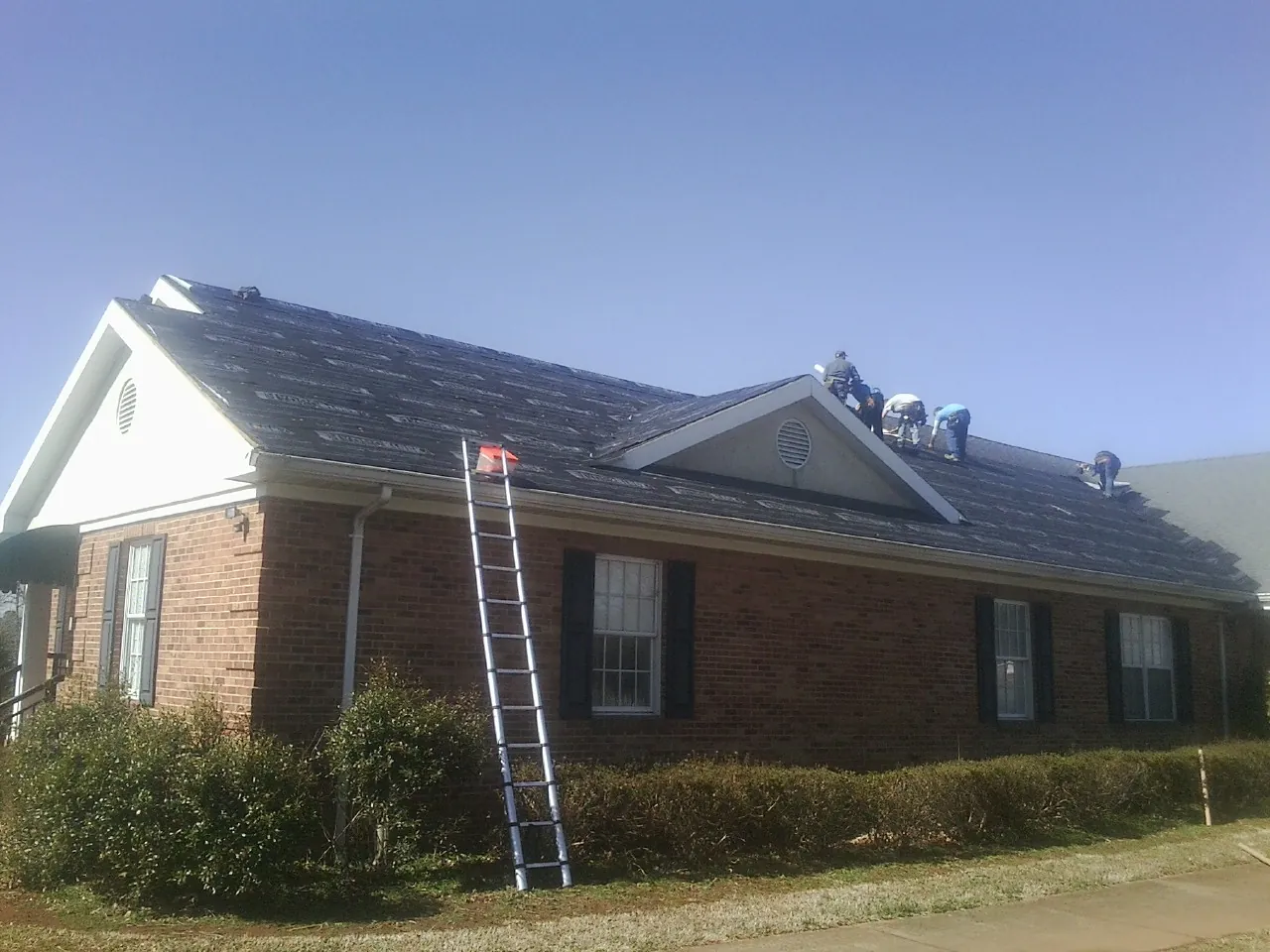Crew tearing shingles off a brick ranch roof with a ladder set — Emergency Roof Repair work by our crew in Saratoga Springs