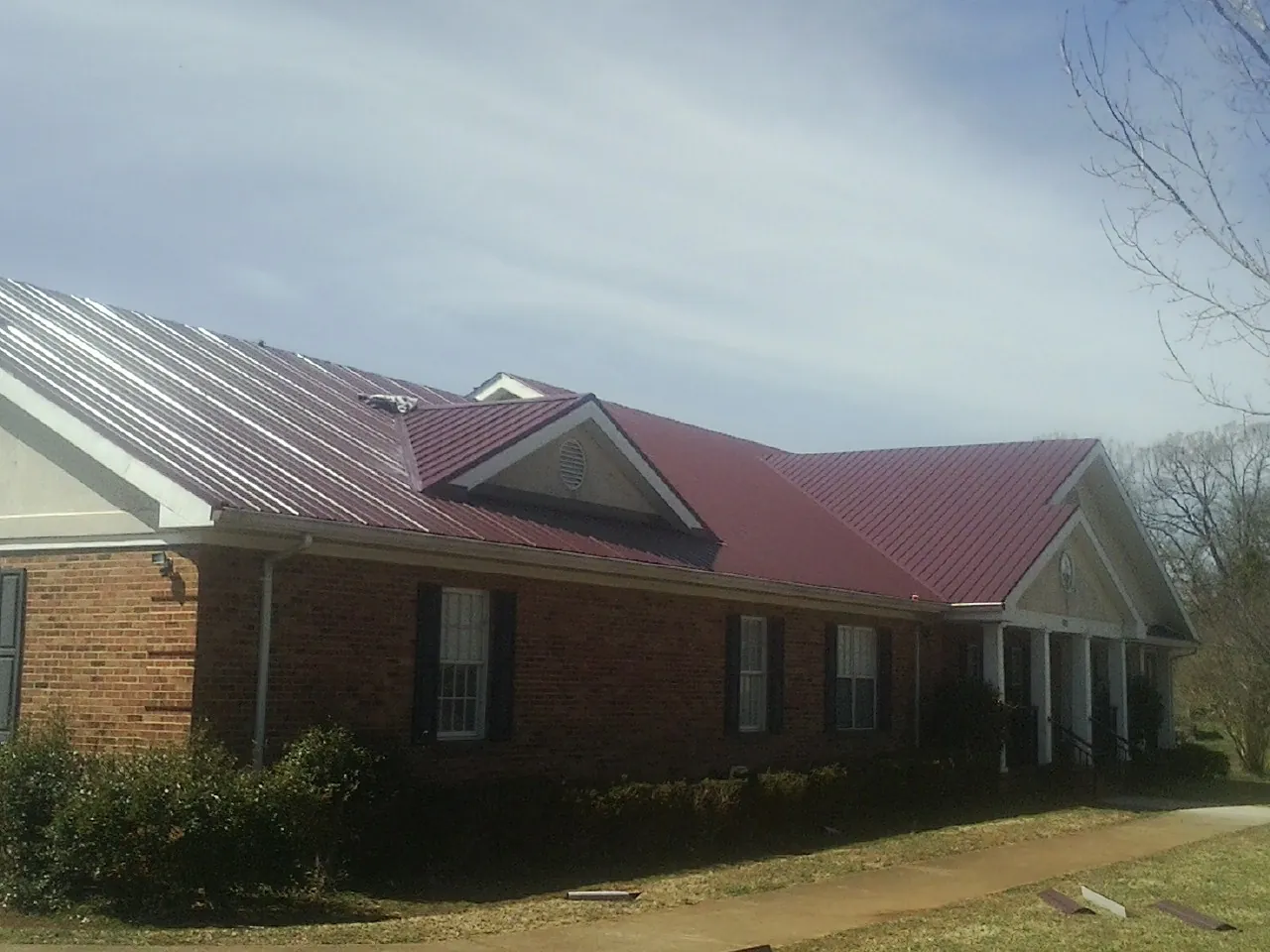 Red metal roof with gabled entries on a long brick building, from a Hail Damage Roof Repair job in Saratoga Springs