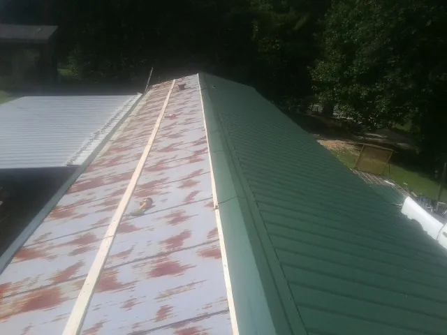 Old rusted panels beside newly installed green metal roofing — Wind Damage Roof Repair by Roofing Brothers in Saratoga Springs