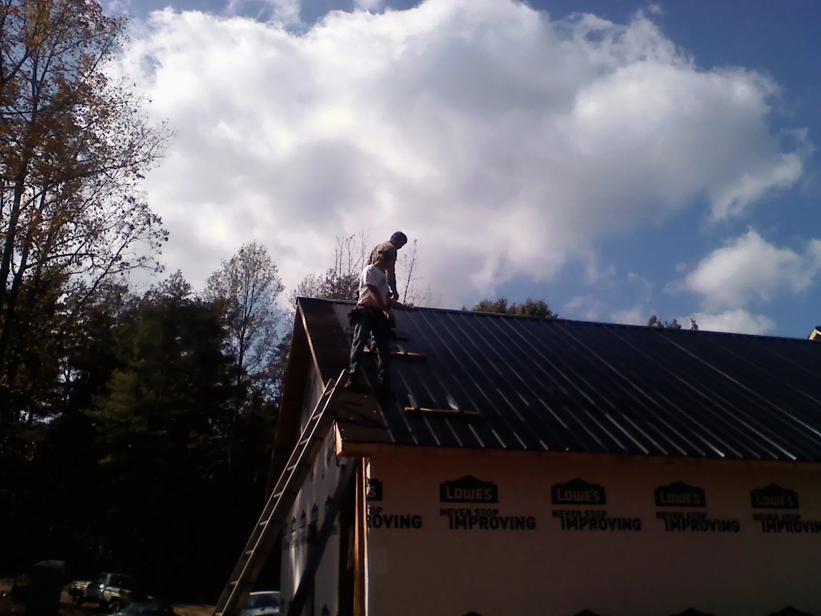 Roofer fastening dark metal panels high against a cloudy sky, from a Roof Inspection job in Saratoga Springs