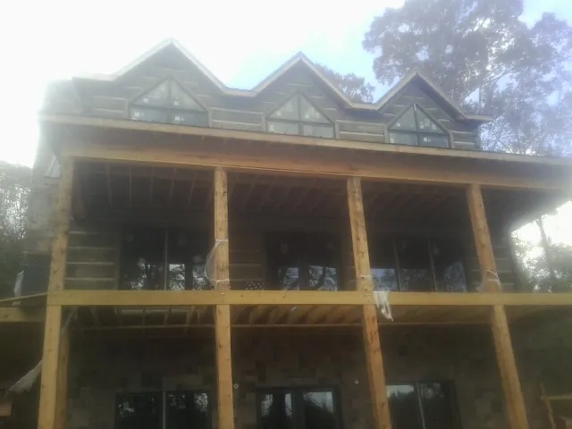 Dormers and porch framing on a large log home under construction — Roof Coating work by our crew in Saratoga Springs