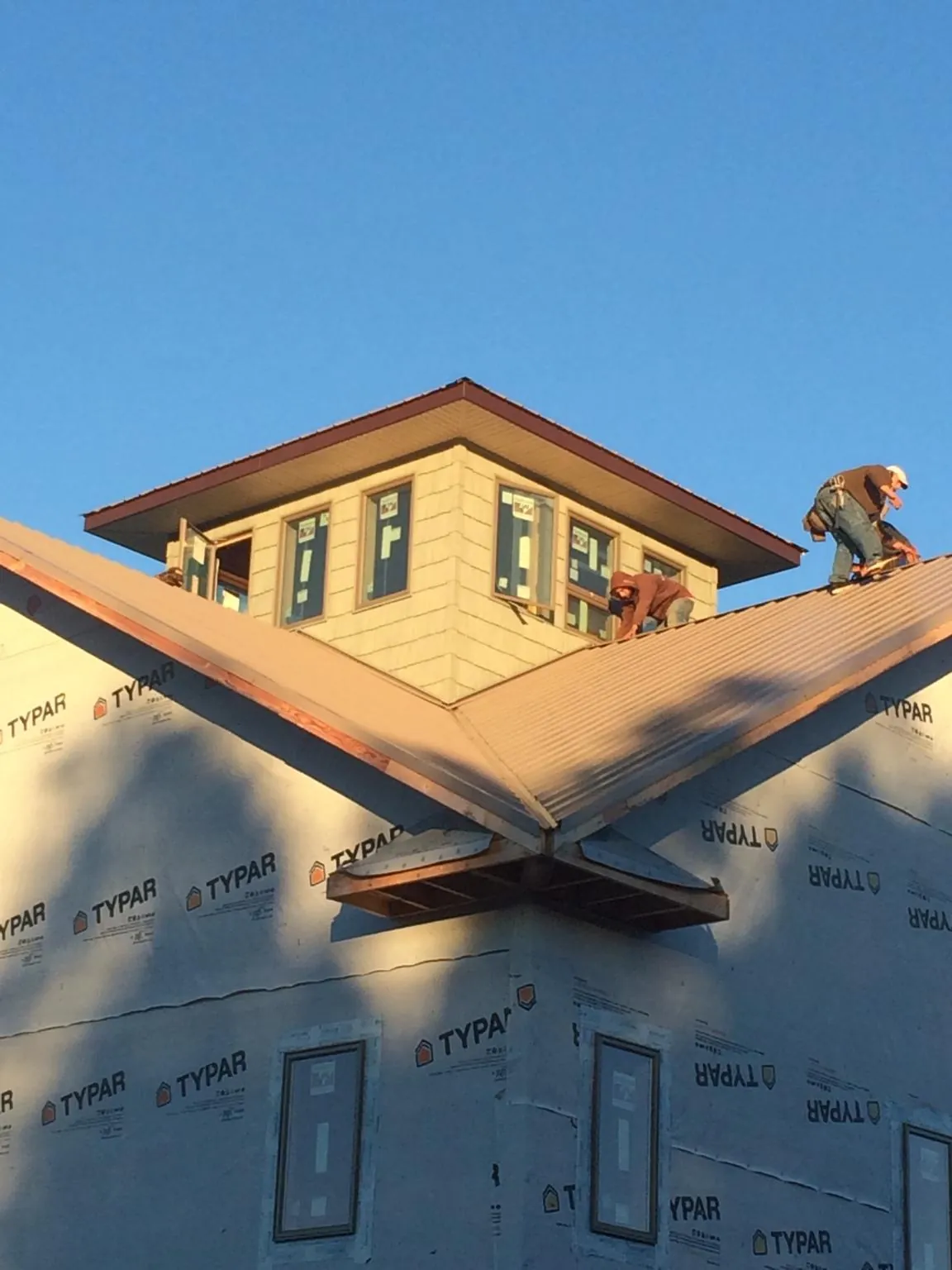 Roofers working around a rooftop cupola on a new metal roof at sunset — Roof Waterproofing in Saratoga Springs by Roofing Brothers